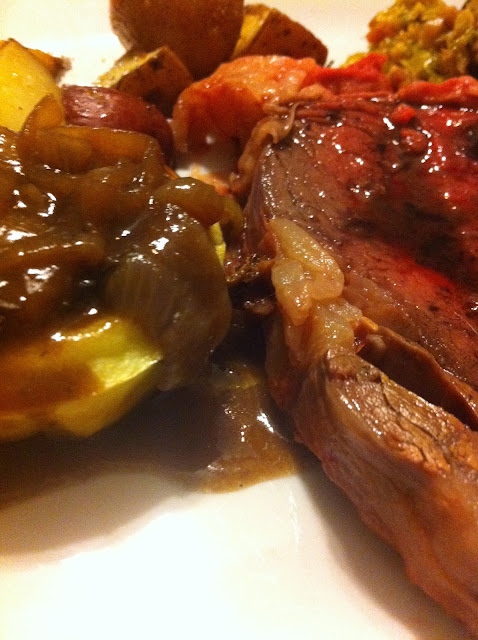 Close-up plate with sliced meat, roasted potatoes, caramelized onions and gravy, warm brown tones